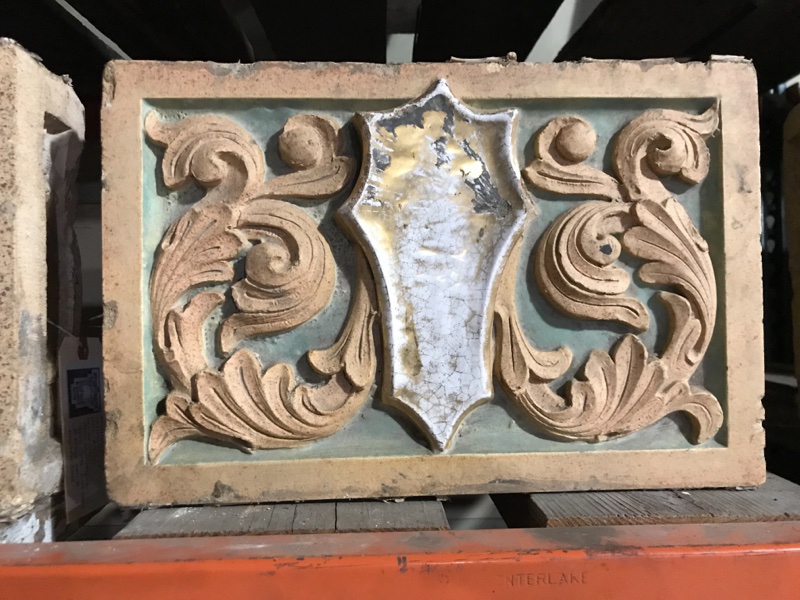 Terra Cotta shield in floral field with polychrome glaze, in green and distressed gold.