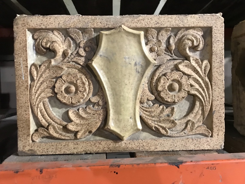 Terra Cotta shield in floral field with polychrome glaze, in green and yellow.