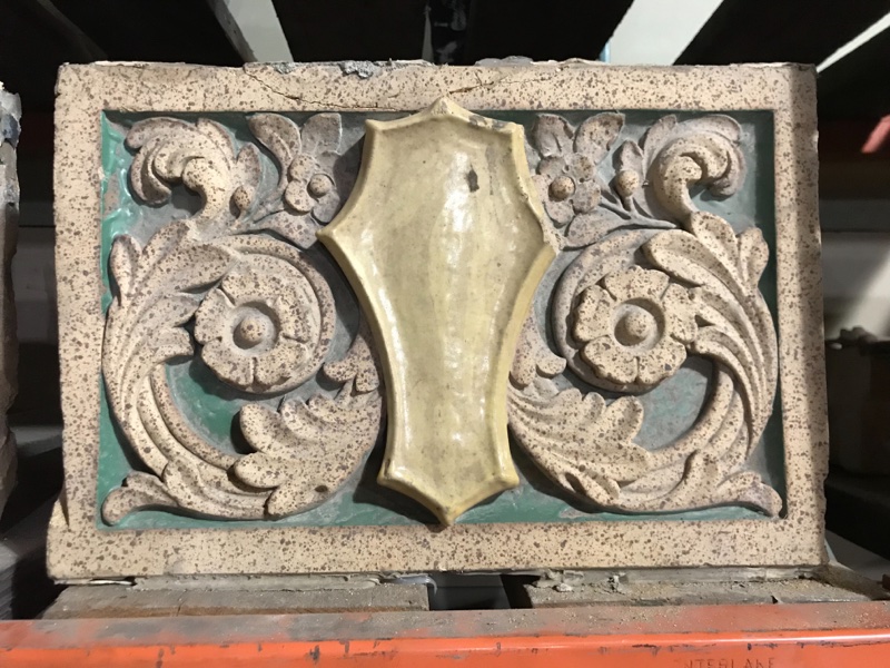 Terra Cotta shield in floral field with polychrome glaze, in green and gold.