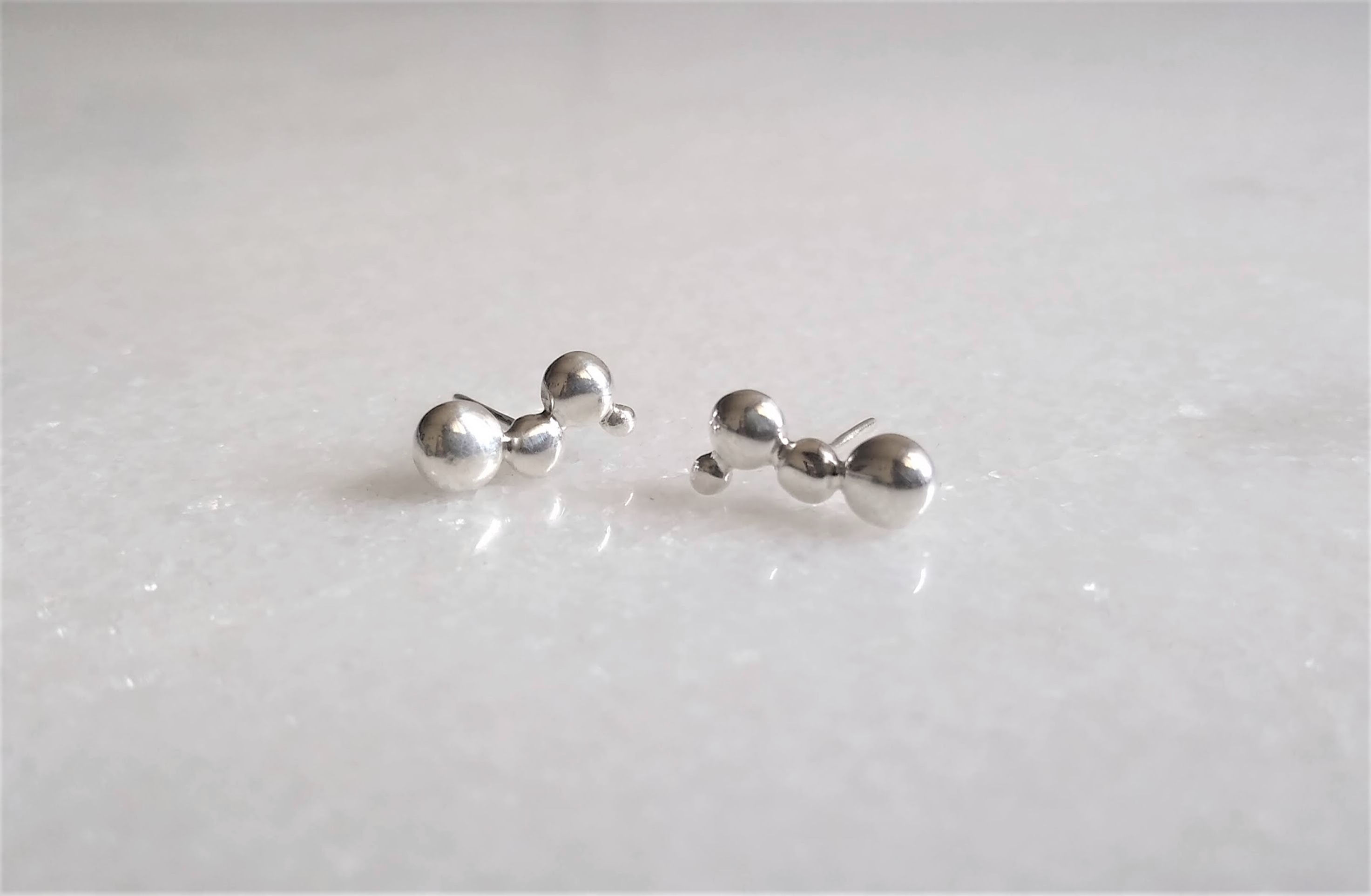 um brinco em prata feito com bolinhas de diferentes tamanhos soldadas juntas em diferentes posições