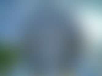 Geodesic sphere against a cloudy sky at Epcot, with a reflective monument in front. Visitors nearby, trees, and blue signage visible.