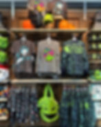 Store display with Halloween-themed apparel and accessories. Features shirts, backpacks, and a green Oogie Boogie bag. Pumpkins decorate shelves.