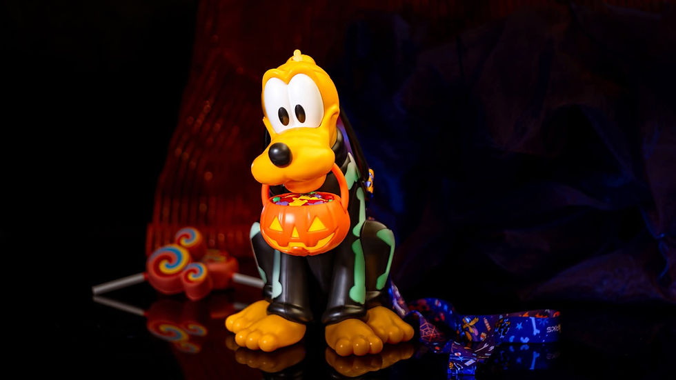 A colorful toy dog holds a pumpkin-shaped candy bucket, surrounded by lollipops. Dark, festive background. Halloween theme.