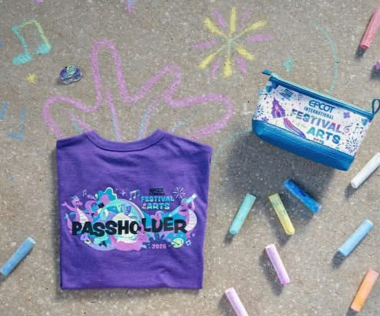Purple T-shirt and pouch with "EPCOT Festival of the Arts" design on chalk-decorated pavement. Pastel chalks scattered around.