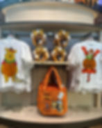 Store display with Halloween-themed merchandise. White shirts feature cartoon characters in pumpkin costumes. Orange bag reads "Happy Halloween." Tiger ear headbands on shelf above.