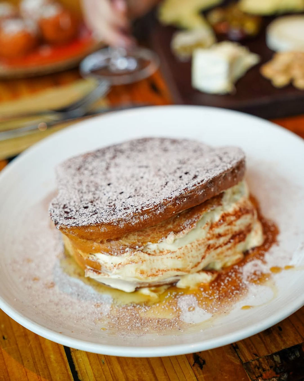 Rich dish resembling tiramisu or stuffed French toast, layered with cream and dusted with powdered sugar and cinnamon, served on a white plate.