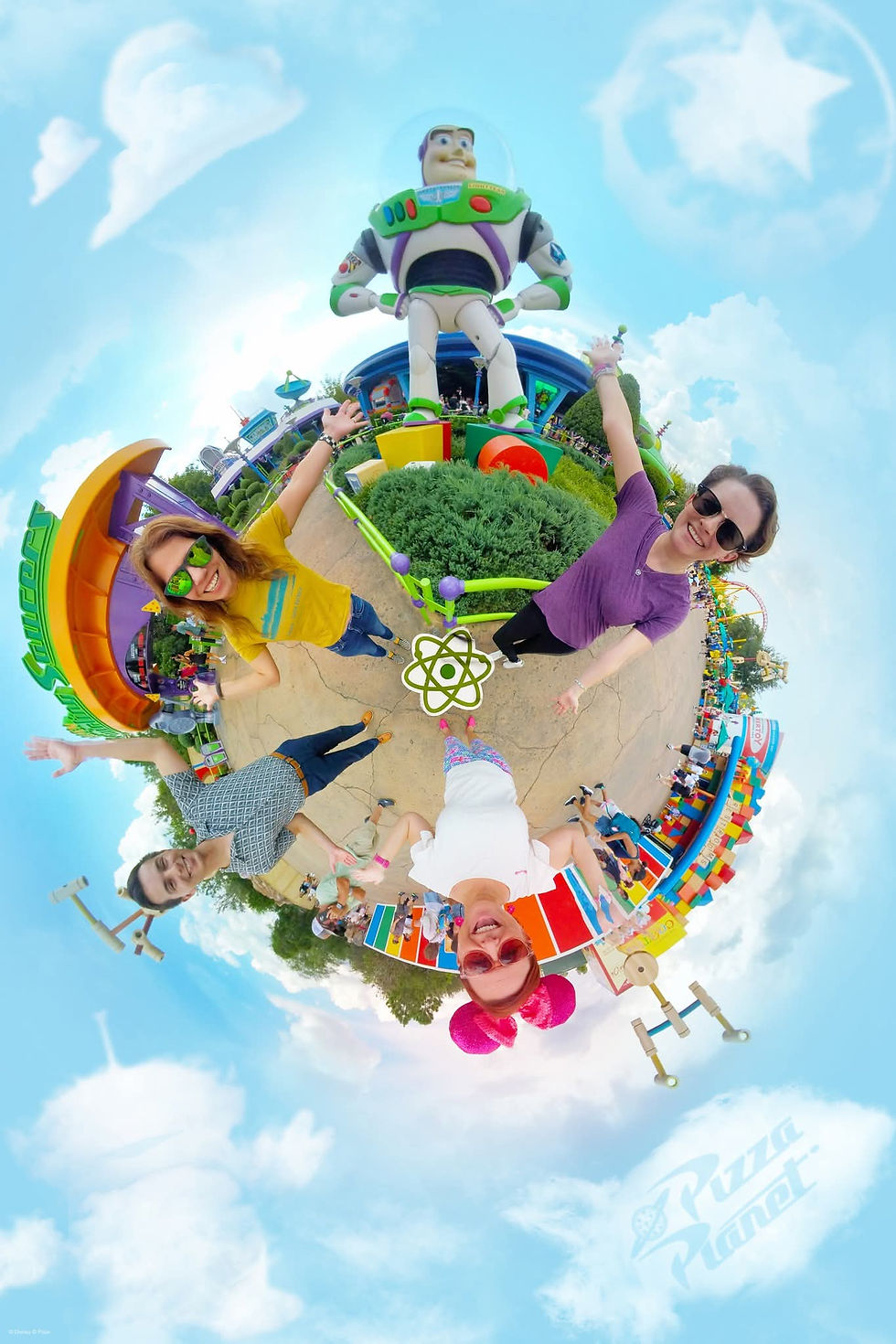 Four people pose excitedly under a giant Buzz Lightyear statue at a theme park. Bright colors and a "Pizza Planet" logo are visible.