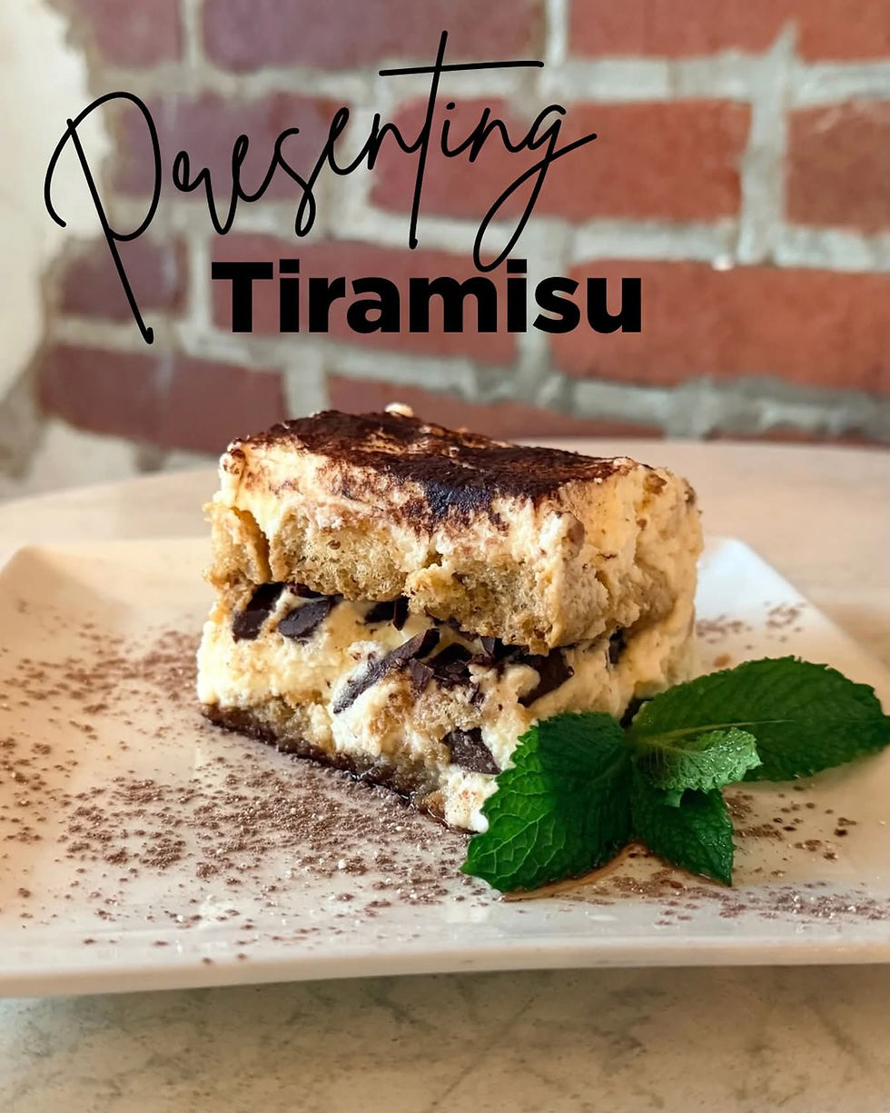 A slice of tiramisu on a white plate dusted with cocoa powder, layered with mascarpone and dark chocolate pieces, garnished with fresh mint leaves, with “Presenting Tiramisu” text overlaid in front of a brick wall background.