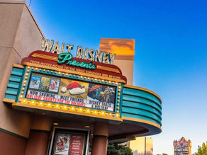 Walt Disney marquee displays holiday shorts ad with colorful lights. Clear blue sky and Hollywood Tower visible in the background.