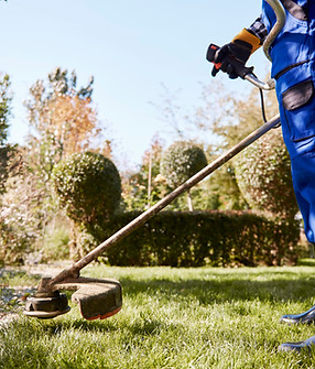 gardener-with-weedwacker-cutting-grass-garden-scaled.jpg