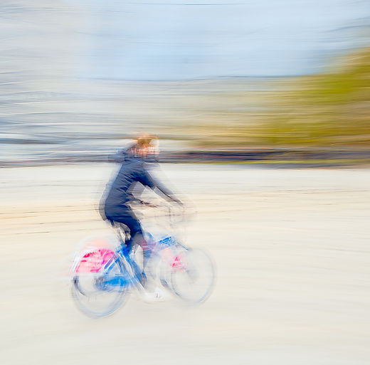 A fine art wall art icm photo print capturing the fleeting motion of a cyclist on an Oslo rent-a-bike. The blurred figure and dynamic composition convey the rhythm and energy of urban life in constant motion.