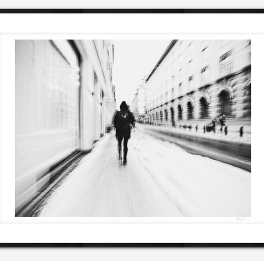 An abstract black-and-white image captures a solitary figure walking up Prinsens gate in Oslo, leaving soft footprints in freshly fallen snow. The blurred motion and wintry stillness evoke themes of solitude, resilience, and quiet introspection in the urban landscape. A Limited Edition Digital Graphic Artwork by Douglas Carr