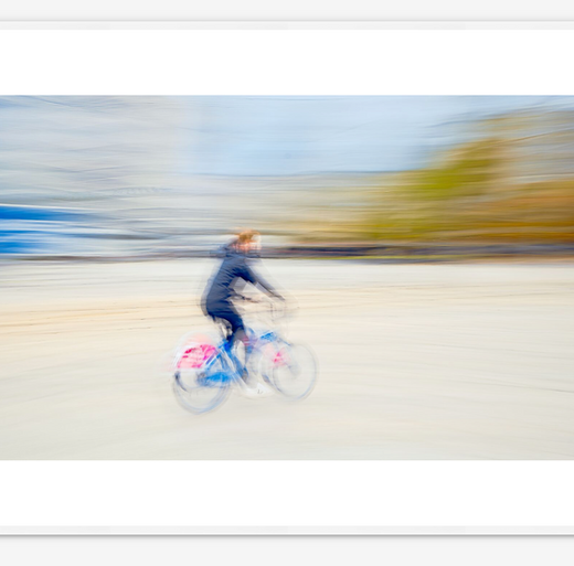 A fine art wall art icm photo print capturing the fleeting motion of a cyclist on an Oslo rent-a-bike. The blurred figure and dynamic composition convey the rhythm and energy of urban life in constant motion.