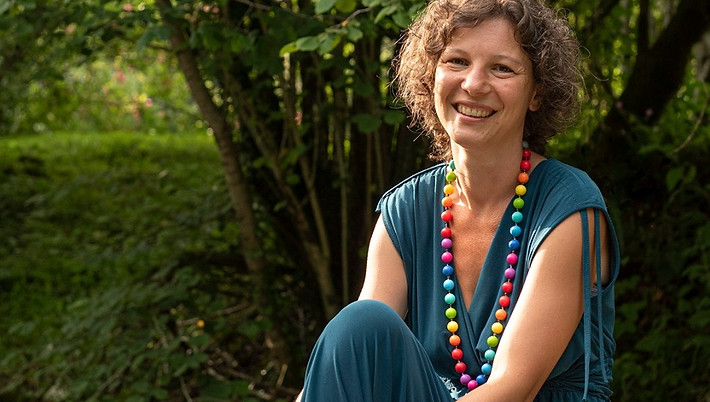 donna che sorride con un abito verde petrolio e una collana arcobaleno