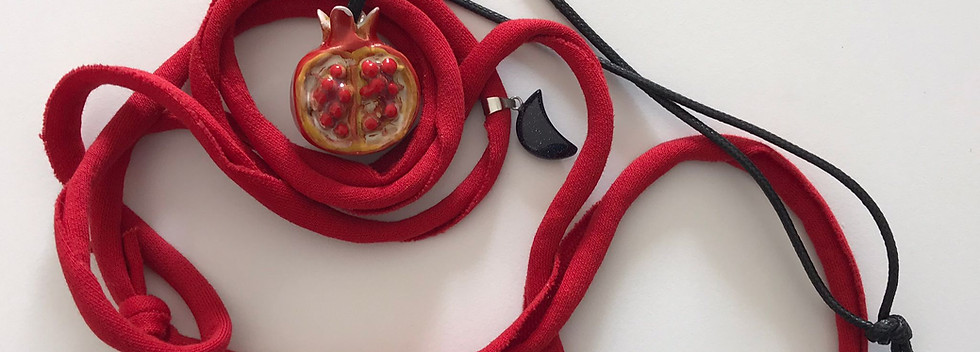 Foto di un nastro rosso aggrovigliato e al centro un ciondolo di ceramica rappresentante un melograno rosso