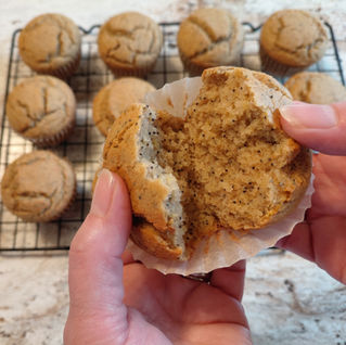 a hand opening a lemon poppy seed muffin with a tray of muffins in the background
