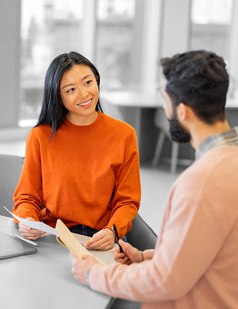 Lady in orange and man in orange blazer sitting down in an office environment and having a meeting