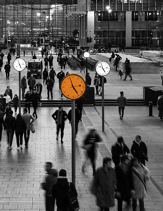 Black and white image of a train station with multiple clocks and many commuters walking in this busy area