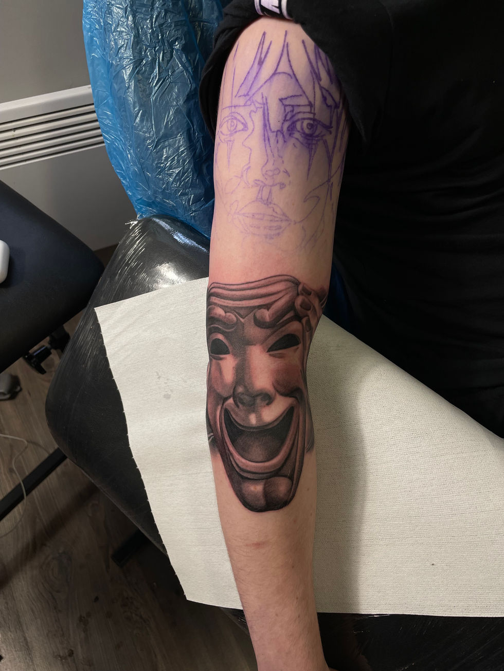 Person's arm with a detailed mask tattoo and unfinished work. Tattoo Amok Prague