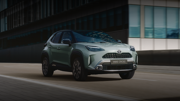 Ein grünes Toyota Yaris Cross Auto fährt auf einer Straße in der Stadt.