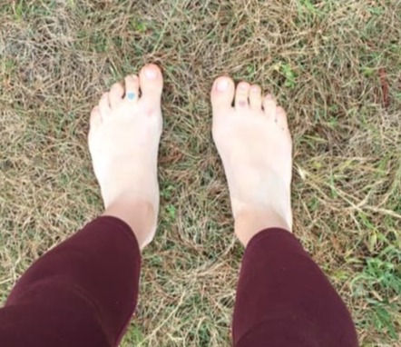 A picture of someone's legs. They are standing barefoot on grass
