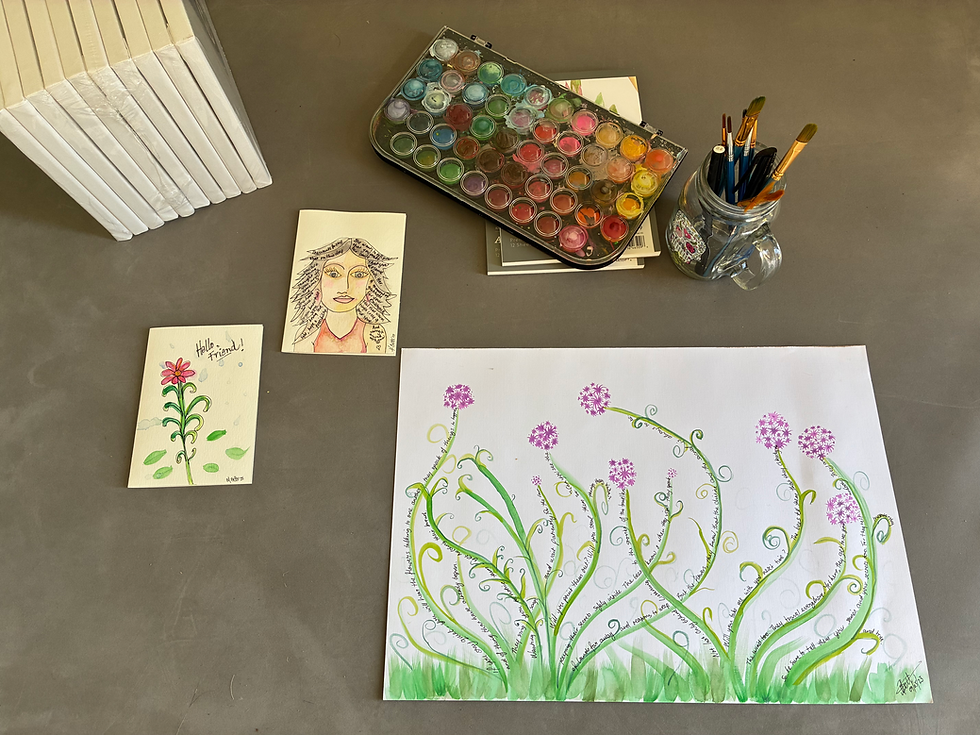 A used palette of watercolour paints, a jar full of pens and brushes, a pack of canvas, two cards and a watercolour painting are spread across a grey background.