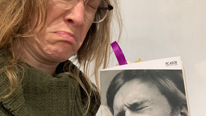 Woman frowning while holding the book "A Little Life" by Hanya Yanagihara. The cover shows a person in distress. She wears glasses and a green sweater.