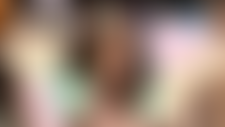 Woman smiling, seated in a cozy room with bookshelves, playfully holding colorful play money. Bright, cheerful setting.