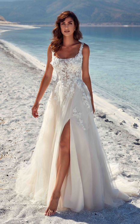 Eddy K wedding gown with slit and square neckline, sleeveless on long haired woman on the beach by the water
