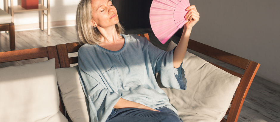 Middle-aged woman managing hot flashes by cooling down with a hand fan near a window