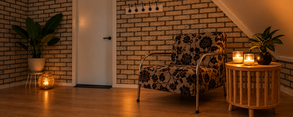 Wachtruimte, aankomstruimte, mooie designer stoel met paarse bloemen en beige stofferingen. Bijzettafeltje met kaarsen en mooie plant. Rechts decoratieve grotere plant op krukje en kaars in mooie bamboe houder.