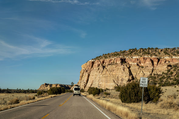 Van driving on a desert road by a large sandstone cliff