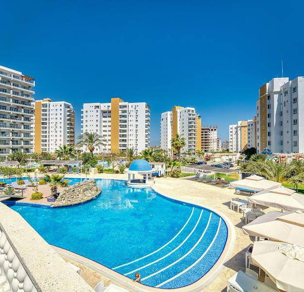Gönnen Sie sich den ultimativen mediterranen Lebensstil mit Ihrem eigenen Stück Paradies in dieser brandneuen Anlage. Sie bietet eine Reihe von Studios Wohnungen mit 1, 2 und 3 Schlafzimmern mit makelloser Präsentation und exklusiven Annehmlichkeiten, nur 600 Meter von atemberaubenden Sandstränden und kristallklarem Wasser entfernt.

Die Wohnungen im makellosen, zeitgenössischen Stil bieten mit ihren hohen Decken, dem herrlichen Tageslicht und der küstennahen Farbpalette ein Gefühl von Leichtigkeit und Komfort. Der elegante Grundriss jedes Designs bietet viel Platz zum Ausstrecken und Entspannen, mit einer voll ausgestatteten Küche und einem Balkon, der sich perfekt für den Morgenkaffee und den Abendwein eignet, während Sie gleichzeitig die malerische Aussicht auf das Resort genießen.

Die Annehmlichkeiten des Resorts sind absolut unübertroffen: wunderschön angelegte Anlagen, mehrere Pools (darunter ein beheizter Innenpool, ein tropischer Pool und ein Aquapark) sowie ein Golfplatz, der bald eröffnet wird. Zahlreiche Bars, Cafés und Restaurants bieten erstklassige kulinarische Erlebnisse und Grillmöglichkeiten laden zu legendären Grillabenden ein.

Legen Sie mit den luxuriösen Spa-Einrichtungen des Resorts Wert auf Gesundheit und Wellness und absolvieren Sie ein lohnendes Training im voll ausgestatteten Fitnessstudio und auf den Sportplätzen mit Kursen, HYFIT-Training und Kampfsport, bevor Sie sich in das luxuriöse Hamam und die Sauna zurückziehen.

Nur 45 Minuten von den Flughäfen Ercan und Larnaca entfernt, ist es so einfach wie nie zuvor, Ihr Haus an der Küste zu erreichen. Um den lokalen Charme zu erleben, können Sie durch das nahegelegene malerische Fischerdorf Boğaz schlendern, am Yachthafen entlangschlendern und in den Restaurants speisen – die perfekte Möglichkeit, zu entspannen und die mediterrane Atmosphäre zu genießen.