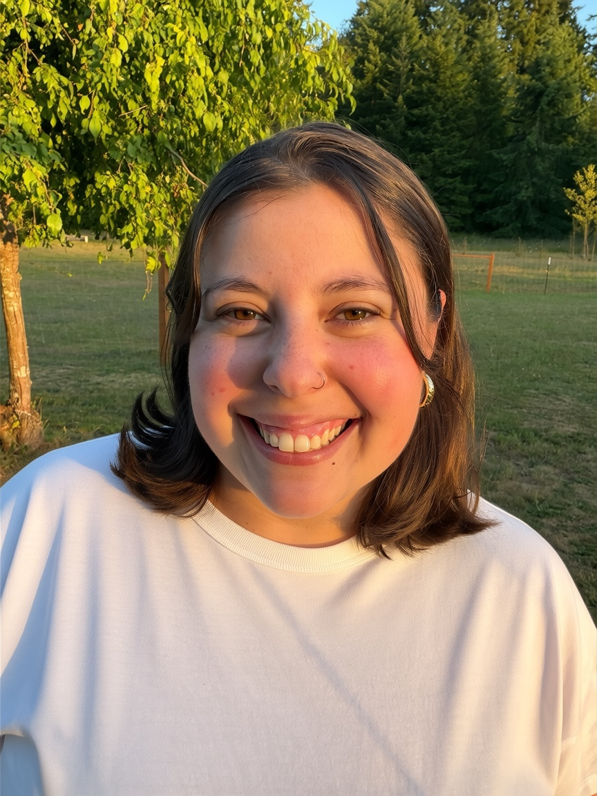 Portrait photo of Callie smiling outdoors in warm evening light, green trees in the background, landscape orientation, friendly and welcoming expression, soft natural colors.