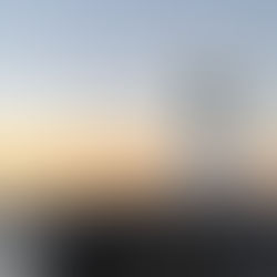 A lighthouse stands on a rocky pier at dawn. The sky is a gradient of orange and blue, with calm waves in the background, creating a serene mood.