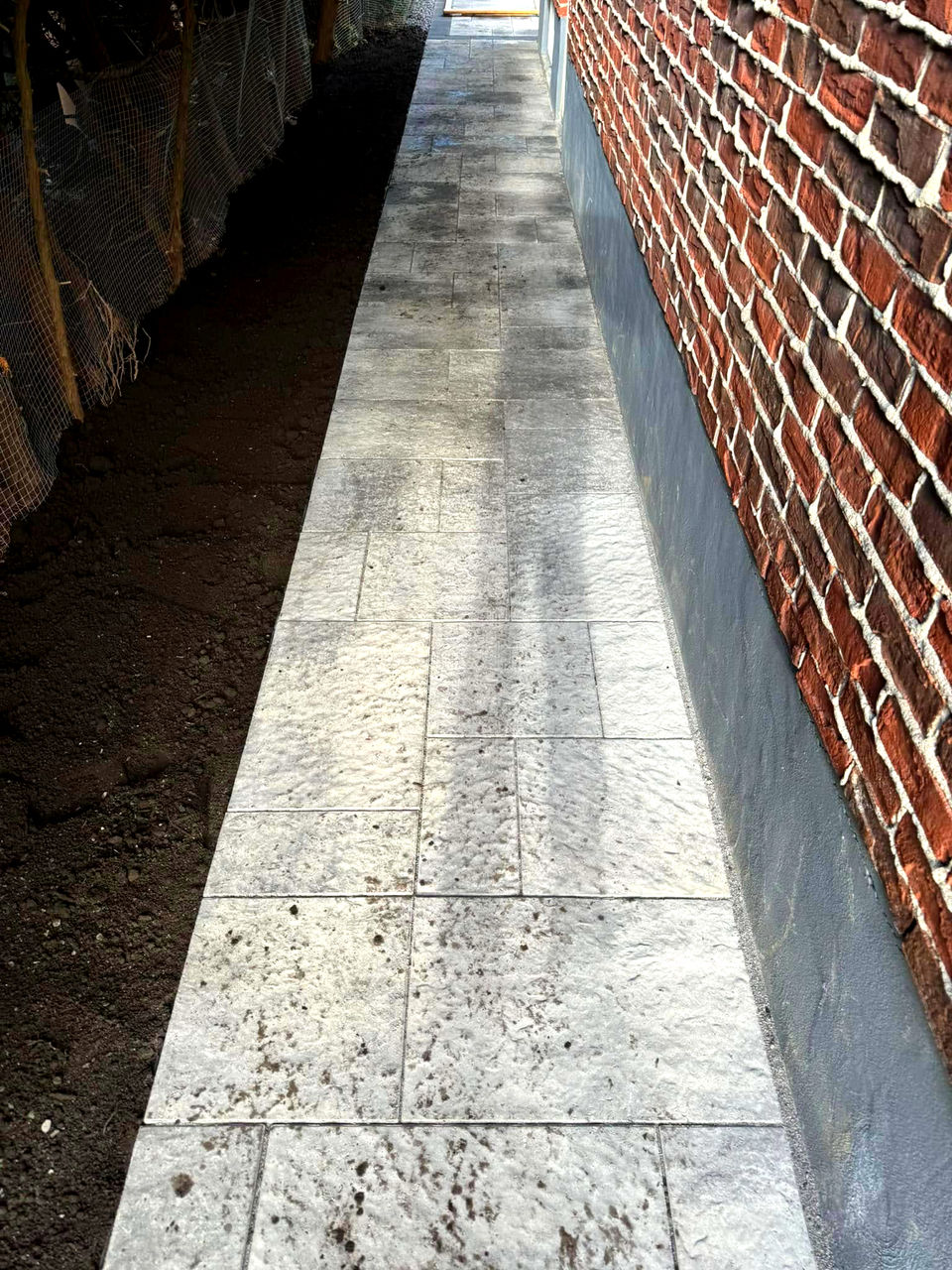 Allée latérale en pavé uni longeant un mur de briques