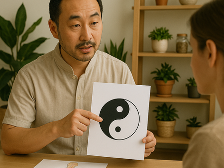 Un praticien de médecine traditionnelle chinoise, d’origine asiatique et d’âge moyen, assis face à une patiente dans un cabinet lumineux décoré de plantes vertes et d’étagères en bois. Il tient une feuille blanche représentant le symbole du Yin et du Yang, tout en le désignant du doigt, tandis qu’un schéma des méridiens du corps humain est posé sur la table devant eux.