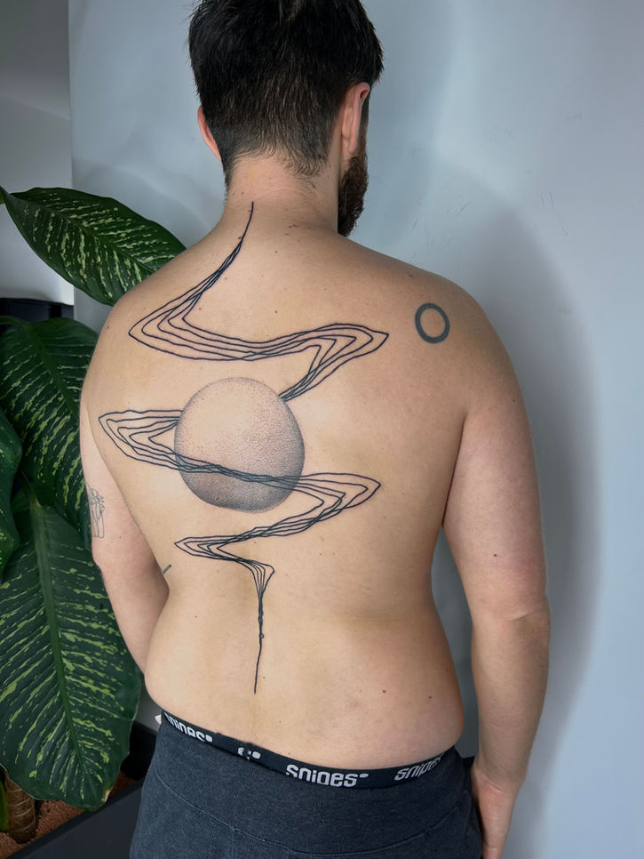 Foto of an abstract back tattoo on the back of a man - a big dotwork circle on the middle with lines swirling around it from the neck to the lower back