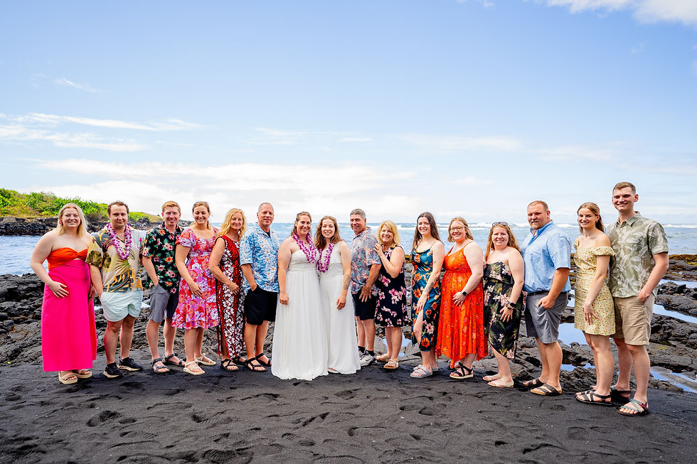 Wedding group portrait on black sand at Punaluu with brides center and smiling guests.