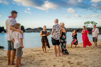 Group gathers on Big Island beach with Kona Wedding Officiant for a heartfelt ceremony, surrounded by ocean, rocks, and tropical skies.