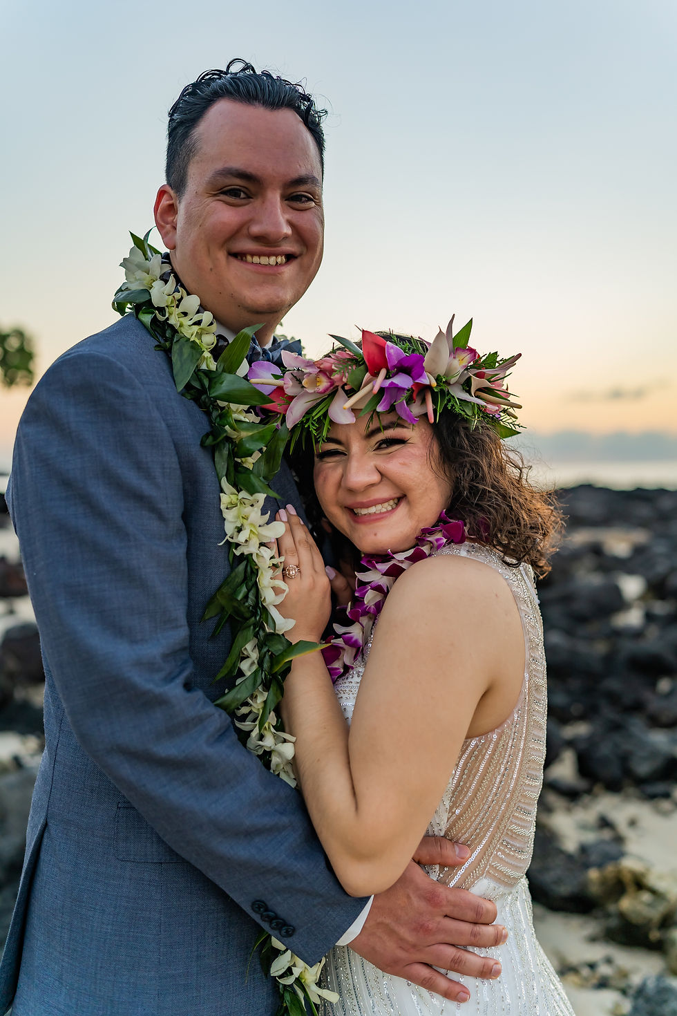 Thumbnail: Two people smile beside Kona’s rocky shore—one in blue suit with floral lei, the other in white dress with flower crown—bathe