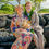 Thumbnail: Couple sits close on Kona’s lava rocks, dressed in floral and light-toned attire with bouquet and leafy lei, framed by tropic