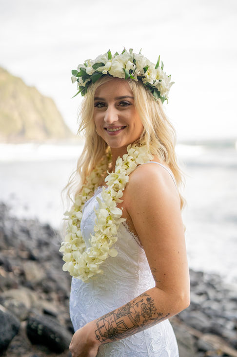 Person in white with flower crown and lei standing near Kona ocean cliffs and waves at sunset