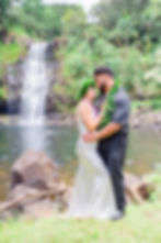 Couple stands by waterfall in Kailua-Kona—Kona Wedding Officiant elopement with vibrant leis, lush f