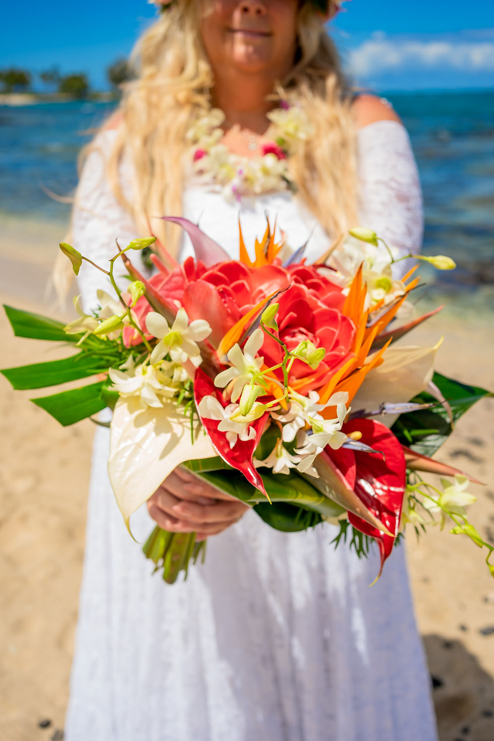 Thumbnail: Bride holds bold tropical bouquet with red, orange, and white blooms on sandy Big Island beach.