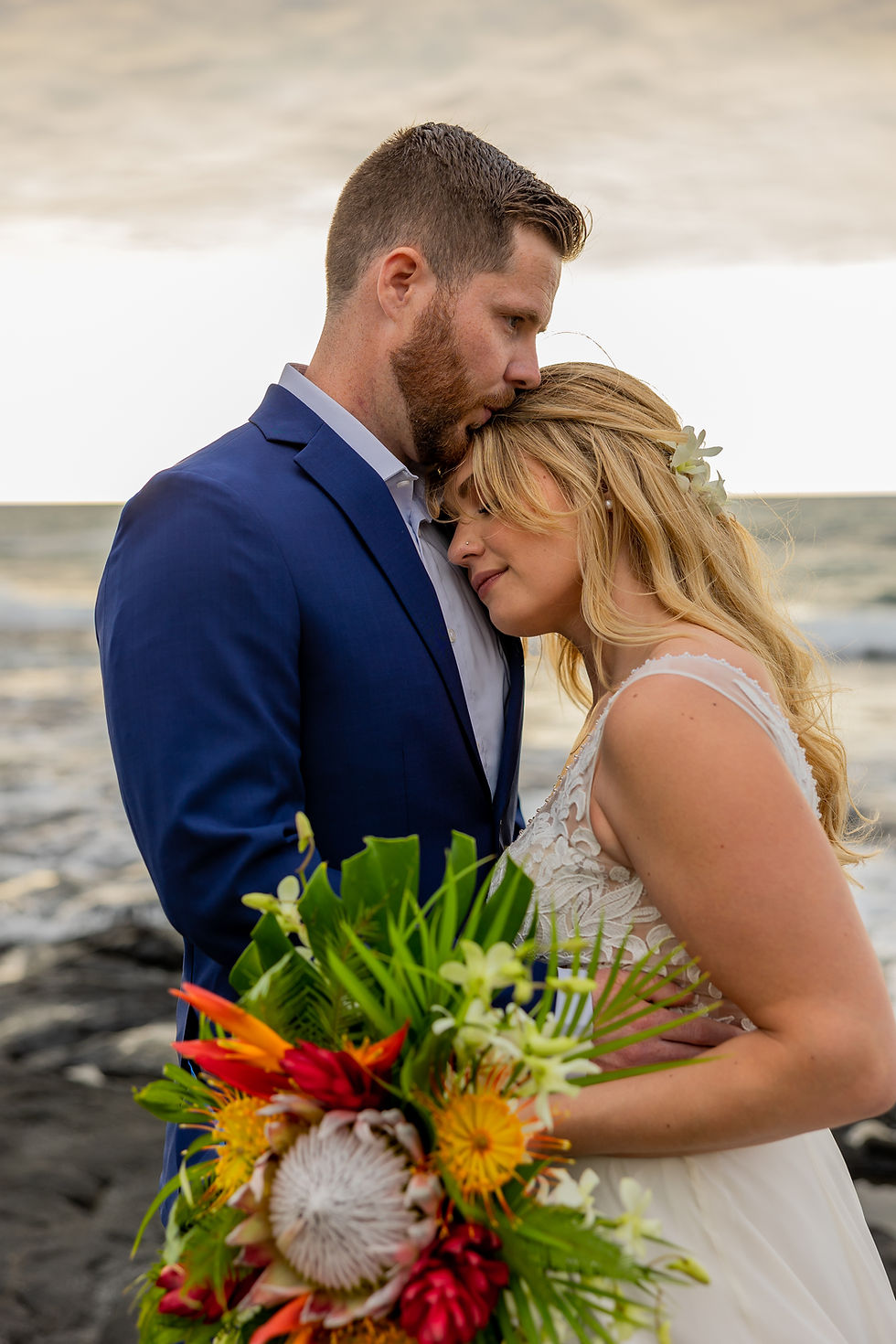 Thumbnail: Groom rests forehead on bride’s head in intimate beachside moment with ocean breeze.