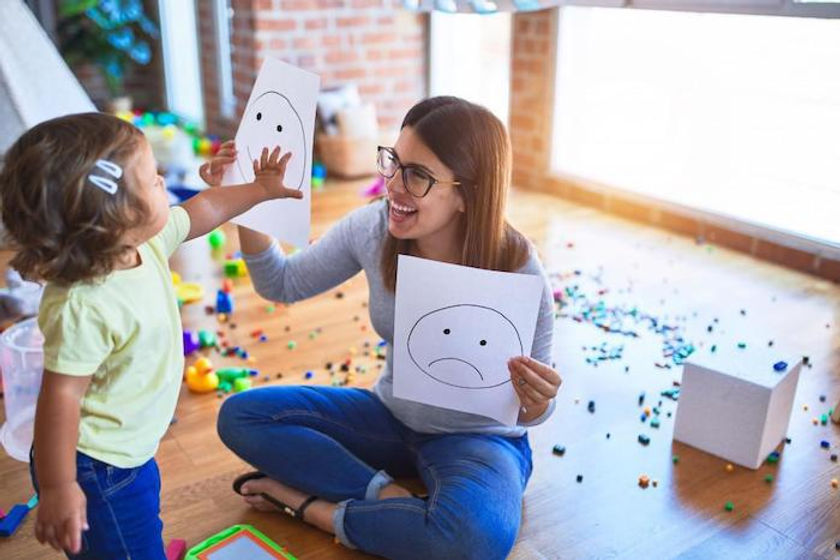 Terapeuta e sua paciente criança brincando com desenhos de expressões faciais