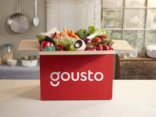 Gousto meal kit delivery box on a kitchen counter, filled with fresh vegetables and ingredients, illustrating convenient home cooking and reduced food waste.