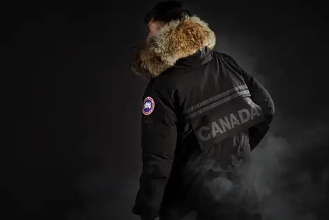 a model wearing a black Canada Goose parka with fur-trimmed hood against a dark background, illustrating premium brand positioning and pricing power.