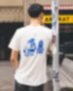 Junger mann lehnt an einen Masten vor einem Dönderladen. Auf seinem weissen Tshirt ist in blau eine Frau abgebildet.